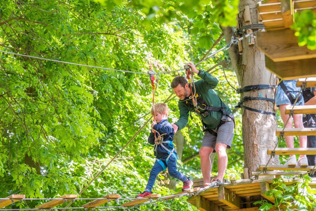 A man guides a young boy on the ropes course at Holkham
